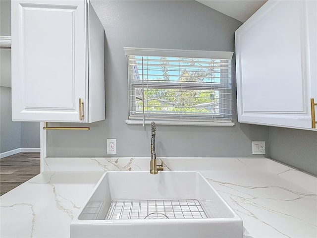 room details featuring white cabinetry, light stone counters, wood finished floors, and a sink