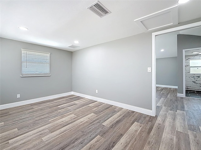 spare room featuring attic access, wood finished floors, visible vents, and baseboards