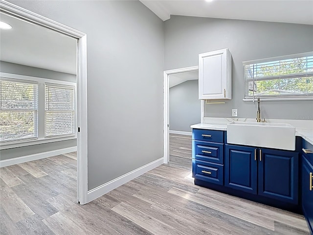 kitchen featuring baseboards, a sink, vaulted ceiling, light wood-style floors, and blue cabinets