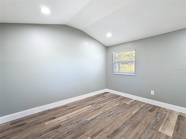 empty room featuring vaulted ceiling, wood finished floors, and baseboards