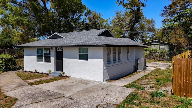 bungalow-style home with central air condition unit, stucco siding, a shingled roof, and fence