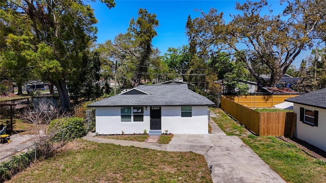 view of front of house featuring a front yard, fence, driveway, stucco siding, and a shingled roof