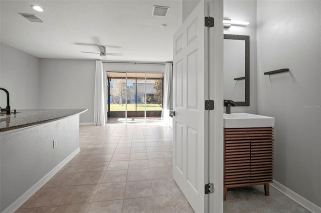 corridor featuring light tile patterned floors, visible vents, baseboards, and a sink