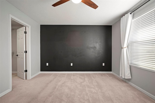 spare room featuring light carpet, baseboards, an accent wall, and a ceiling fan