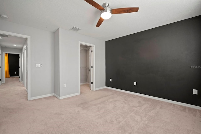 unfurnished bedroom with visible vents, light carpet, baseboards, ceiling fan, and a spacious closet