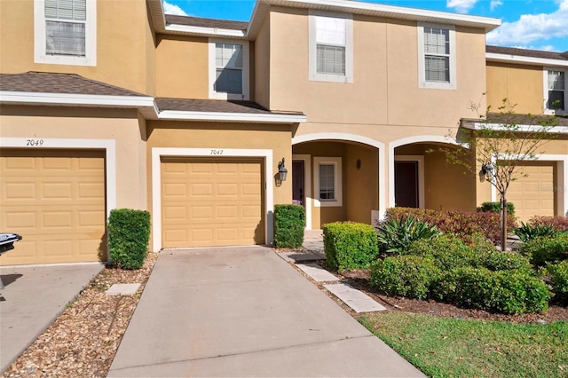 multi unit property with stucco siding, driveway, a garage, and roof with shingles