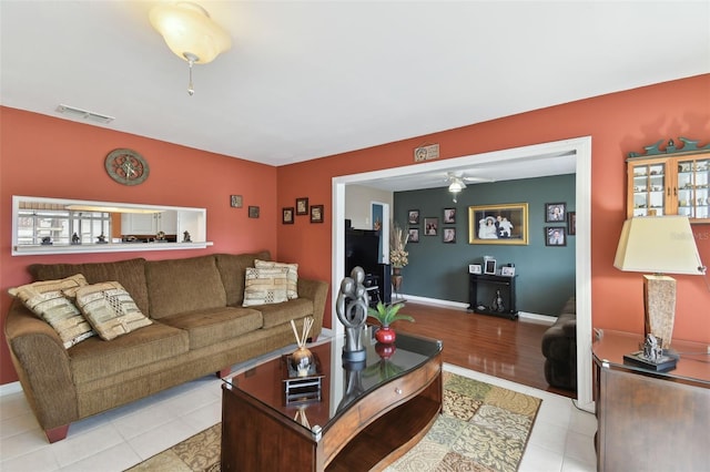 living room with light tile patterned floors, visible vents, baseboards, and a ceiling fan