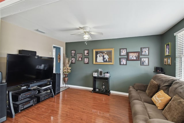 living area with baseboards, wood finished floors, visible vents, and ceiling fan