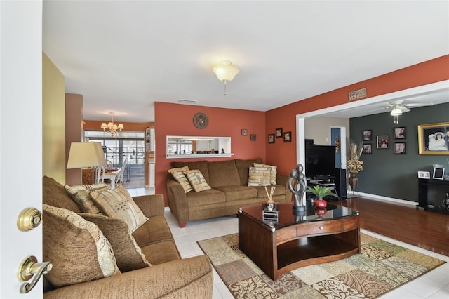 living room featuring light tile patterned floors, visible vents, baseboards, and ceiling fan with notable chandelier