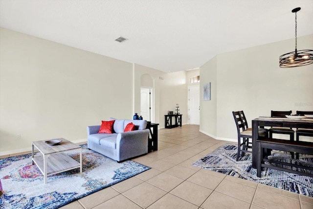 living area featuring visible vents, arched walkways, light tile patterned floors, baseboards, and a chandelier