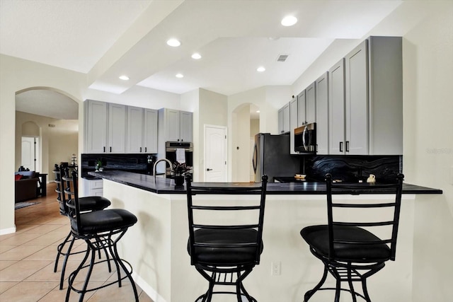 kitchen featuring arched walkways, gray cabinets, stainless steel appliances, a peninsula, and visible vents