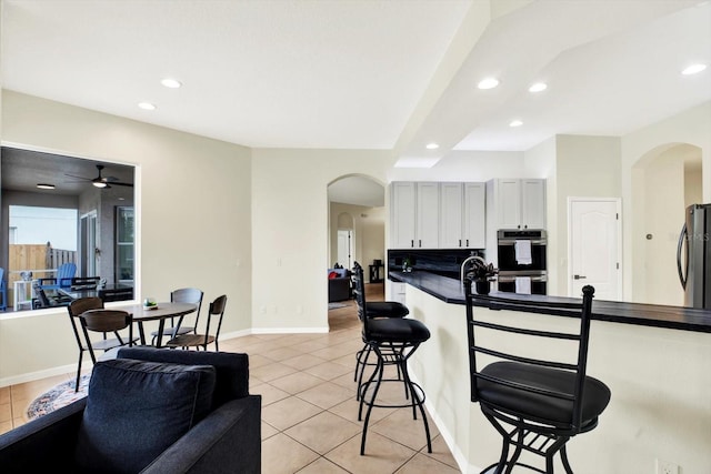 kitchen featuring dark countertops, arched walkways, a kitchen breakfast bar, freestanding refrigerator, and light tile patterned floors