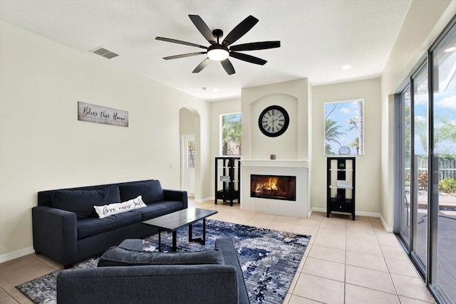 living room with light tile patterned flooring, arched walkways, a large fireplace, a ceiling fan, and visible vents