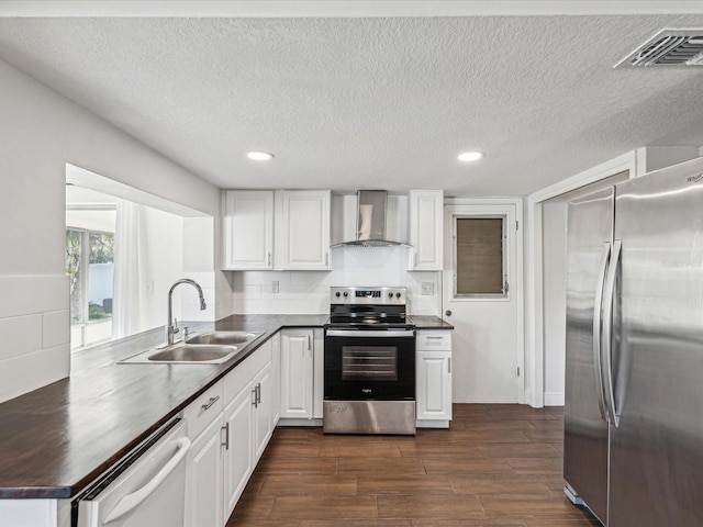 kitchen featuring visible vents, a sink, dark countertops, appliances with stainless steel finishes, and wall chimney range hood