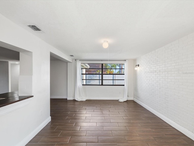 empty room featuring visible vents, brick wall, baseboards, and wood tiled floor