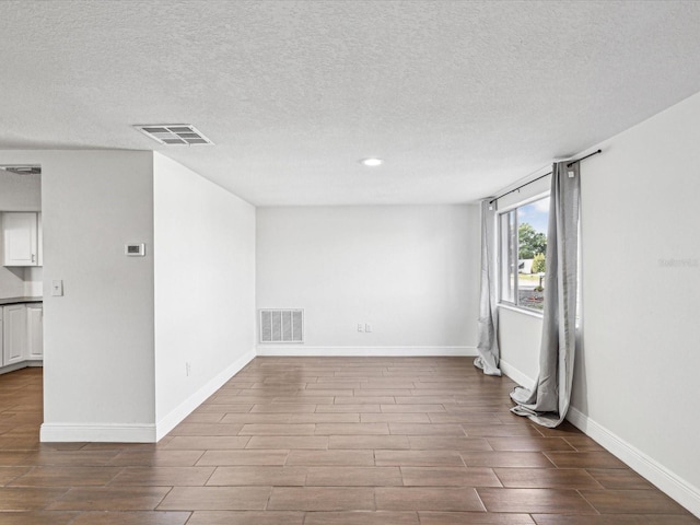 unfurnished room with wood finish floors, visible vents, baseboards, and a textured ceiling