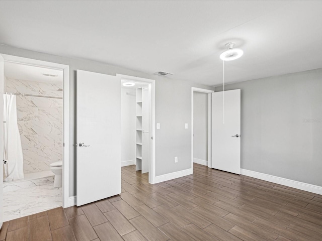 unfurnished bedroom with a spacious closet, visible vents, wood finish floors, a closet, and ensuite bath