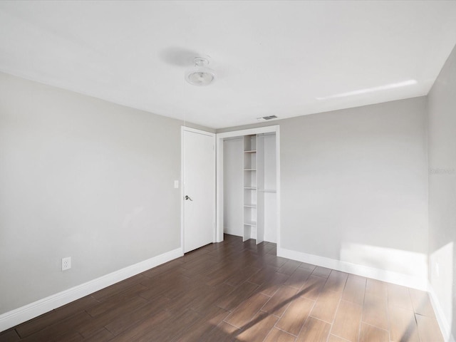 empty room featuring dark wood-type flooring, visible vents, and baseboards