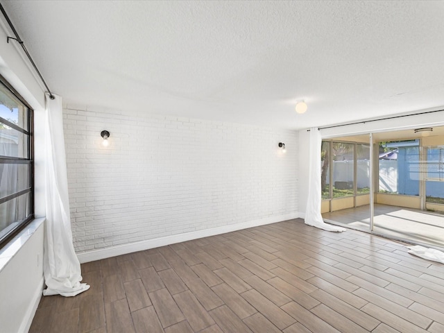 empty room with brick wall, a textured ceiling, and wood finished floors