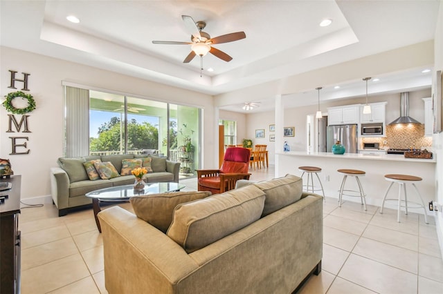 living area with a tray ceiling, light tile patterned flooring, and a ceiling fan