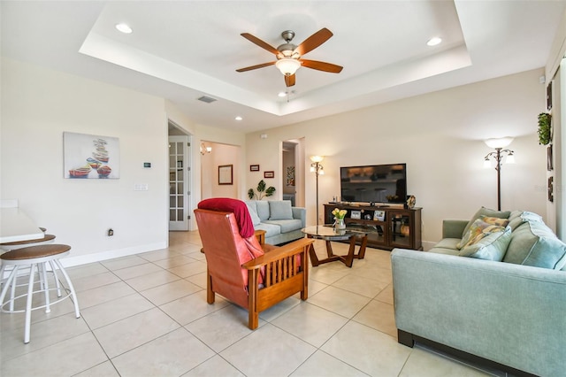 living area featuring a raised ceiling, light tile patterned flooring, baseboards, and ceiling fan