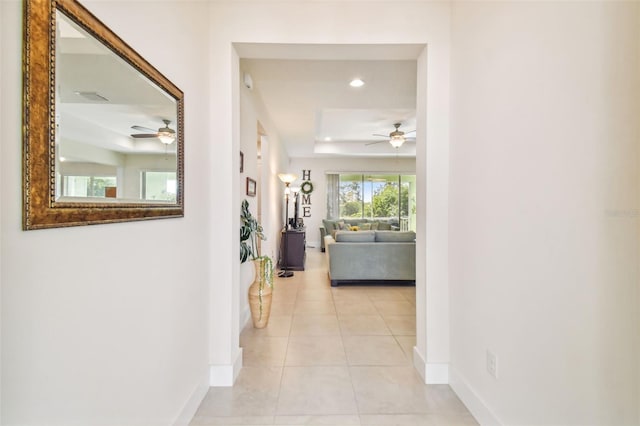 corridor featuring light tile patterned floors, a tray ceiling, baseboards, and recessed lighting