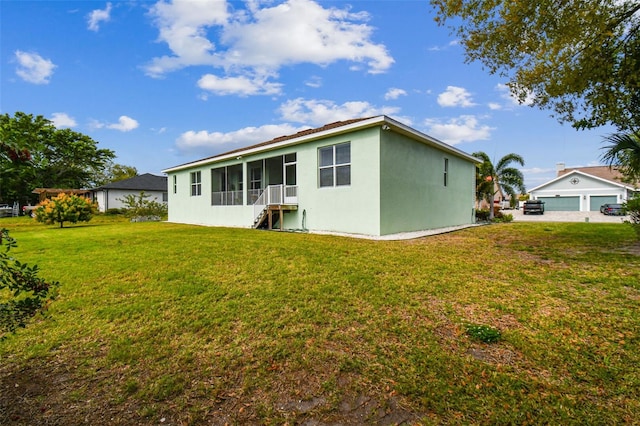 rear view of property featuring a detached garage, a yard, a sunroom, and stucco siding