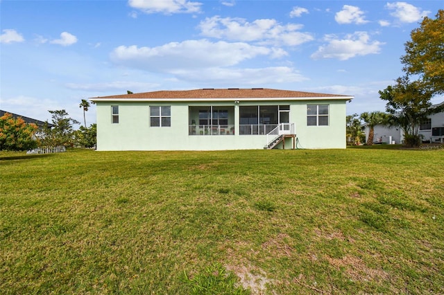 rear view of house with stucco siding, a yard, and a sunroom