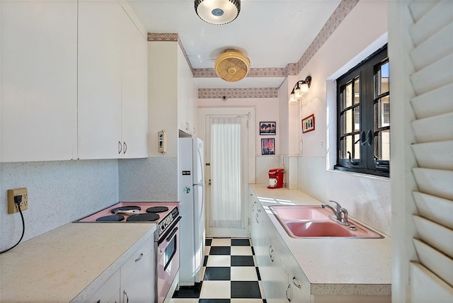 kitchen with a sink, white appliances, tile patterned floors, and white cabinetry