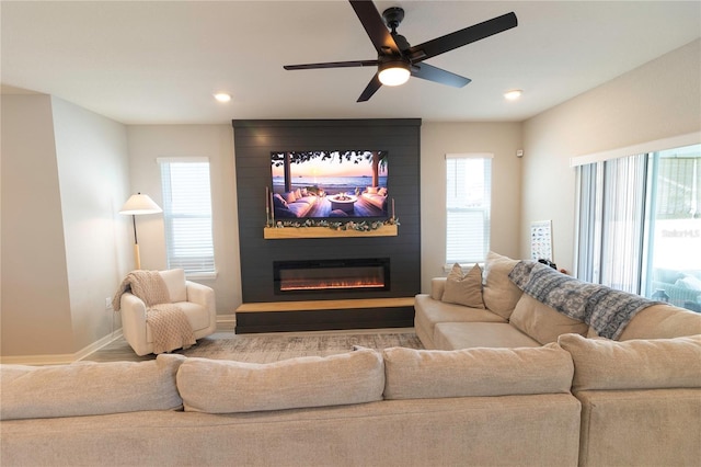 living area featuring a large fireplace, plenty of natural light, baseboards, and a ceiling fan