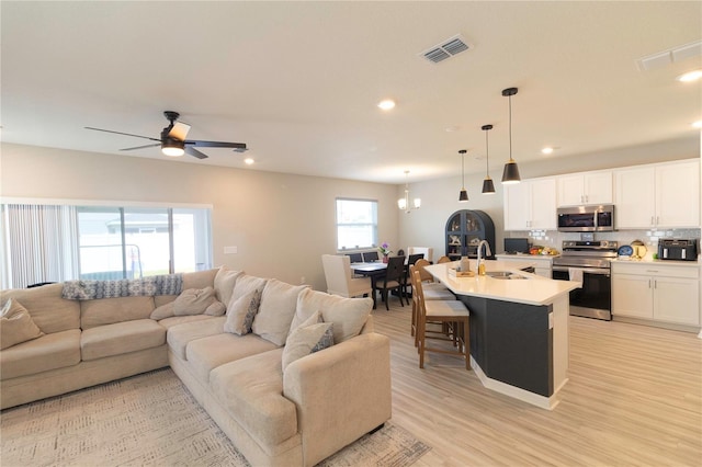 living room featuring recessed lighting, light wood-style flooring, ceiling fan with notable chandelier, and visible vents