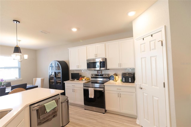 kitchen featuring stainless steel appliances, white cabinets, light countertops, decorative backsplash, and hanging light fixtures