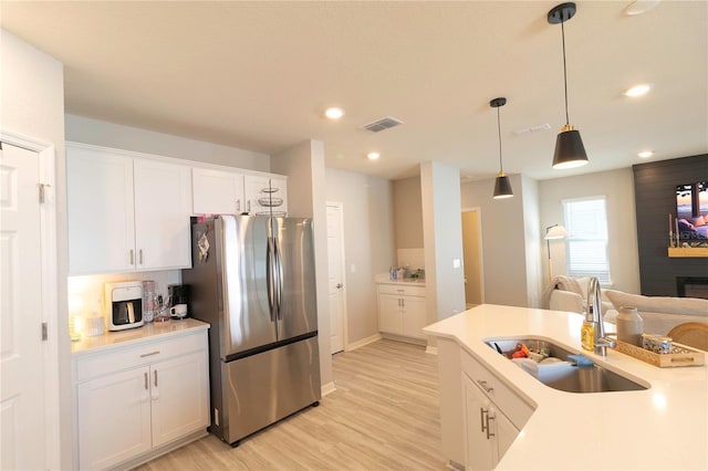 kitchen featuring visible vents, light wood finished floors, freestanding refrigerator, a sink, and white cabinetry