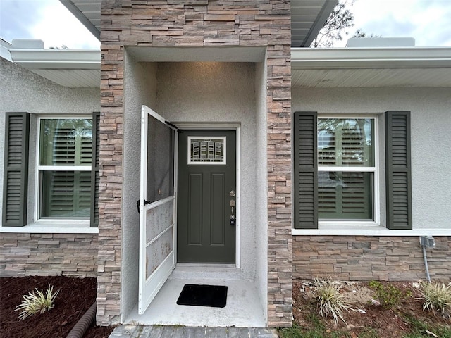 doorway to property featuring stone siding and stucco siding