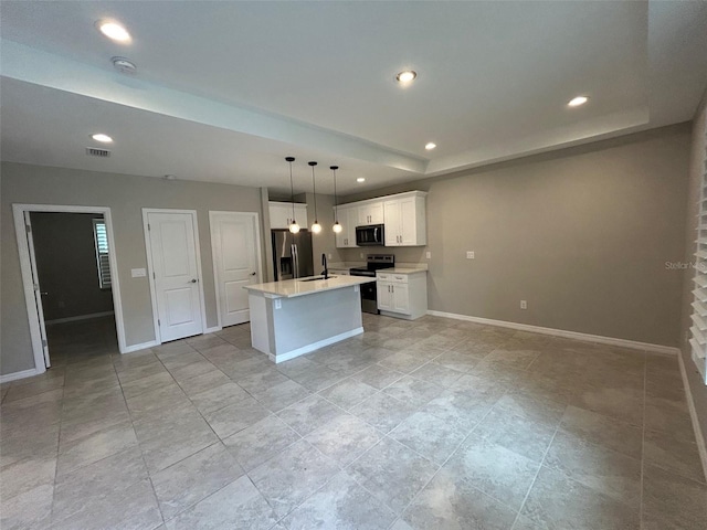 kitchen featuring an island with sink, a tray ceiling, stainless steel appliances, white cabinets, and baseboards