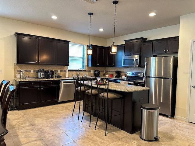 kitchen featuring a kitchen island, a breakfast bar area, light stone counters, appliances with stainless steel finishes, and hanging light fixtures