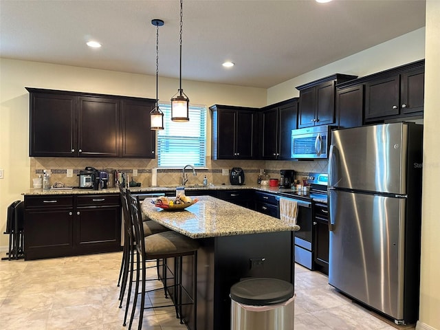 kitchen with a sink, light stone counters, tasteful backsplash, stainless steel appliances, and a breakfast bar area