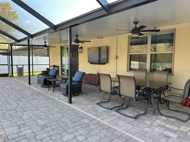 view of patio featuring glass enclosure, a ceiling fan, and fence