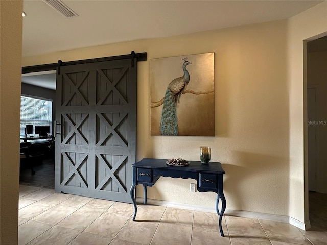 hall with tile patterned floors, visible vents, baseboards, and a barn door