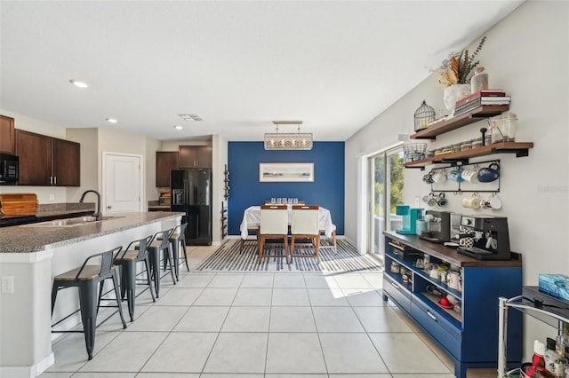 kitchen featuring visible vents, black appliances, a sink, a breakfast bar area, and dark brown cabinets