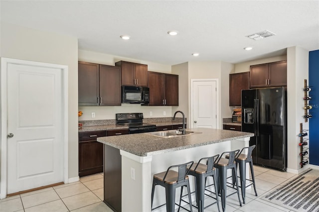 kitchen with visible vents, black appliances, a sink, dark brown cabinetry, and a breakfast bar area