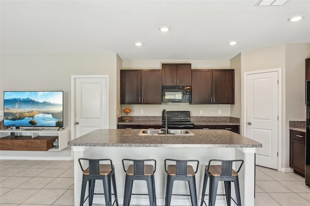 kitchen with black appliances, a breakfast bar, a sink, dark brown cabinetry, and light tile patterned floors