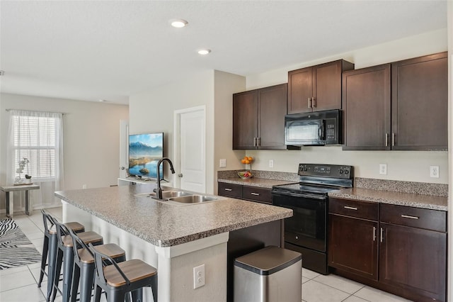 kitchen with light tile patterned floors, a center island with sink, a breakfast bar, a sink, and black appliances