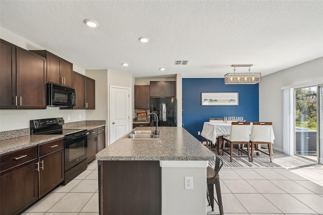 kitchen with black appliances, a sink, a breakfast bar area, light tile patterned flooring, and dark brown cabinets