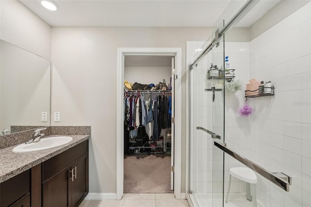 full bathroom with tile patterned flooring, a shower stall, vanity, and a walk in closet