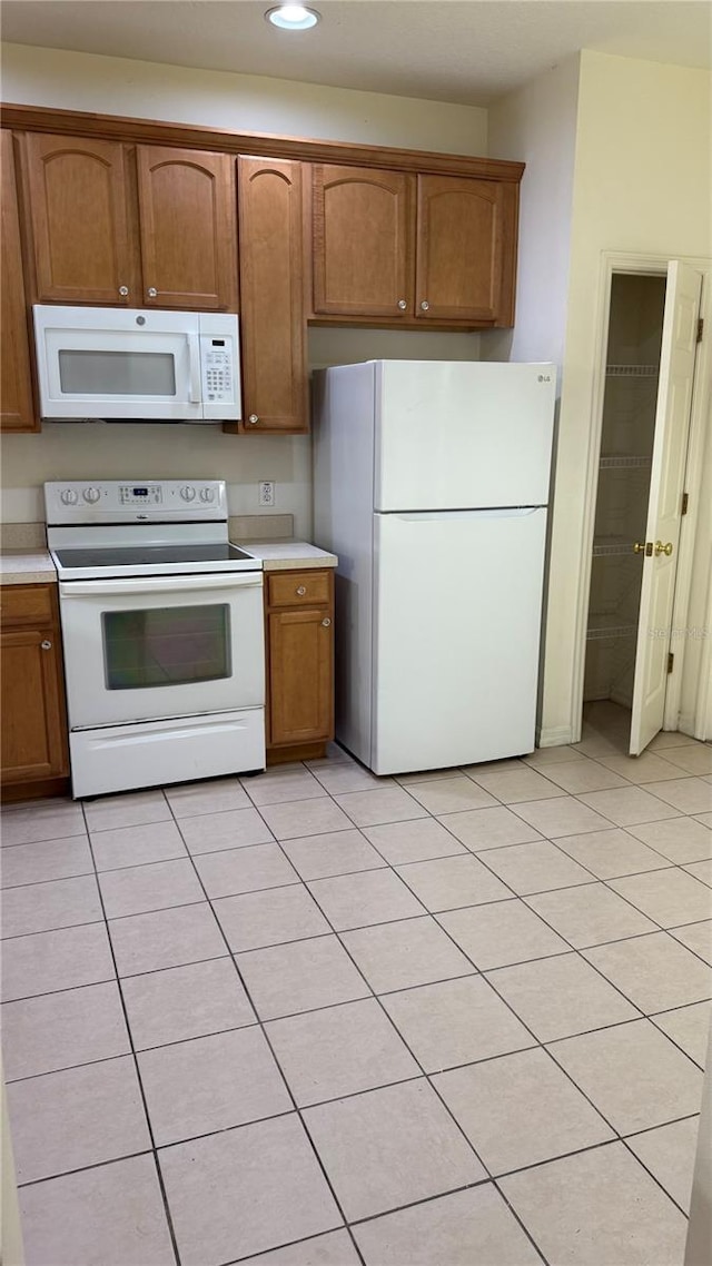 kitchen with light countertops, recessed lighting, brown cabinets, light tile patterned flooring, and white appliances