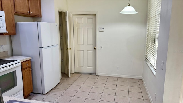 kitchen featuring light tile patterned floors, white appliances, brown cabinetry, and hanging light fixtures