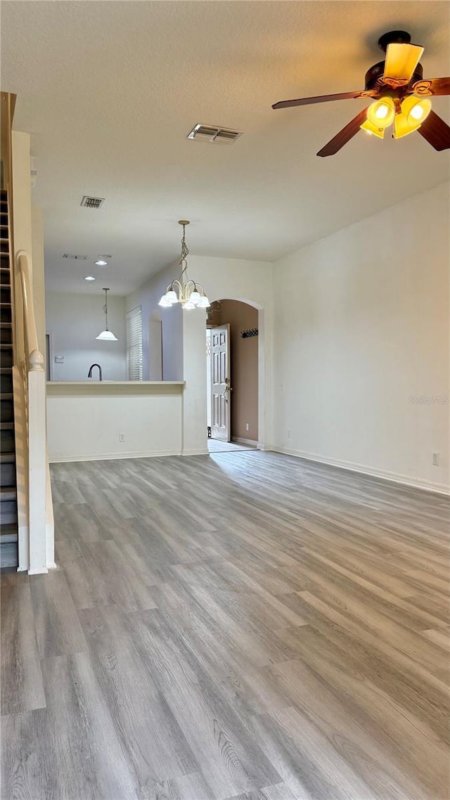 unfurnished living room featuring visible vents, arched walkways, wood finished floors, and ceiling fan with notable chandelier