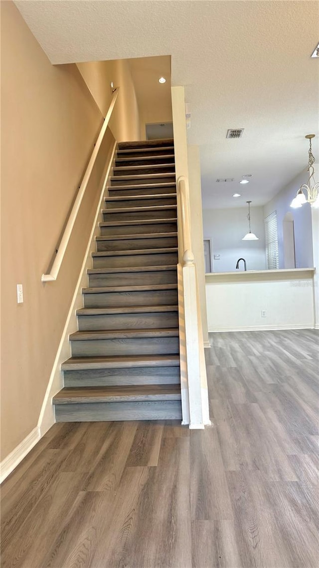 stairway featuring a chandelier, a textured ceiling, baseboards, and wood finished floors