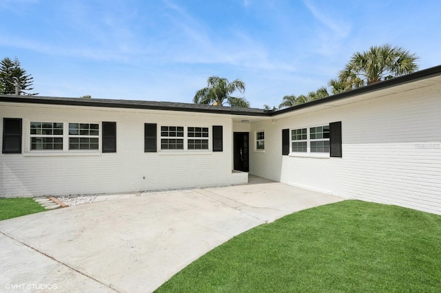 doorway to property with a patio, a yard, and brick siding